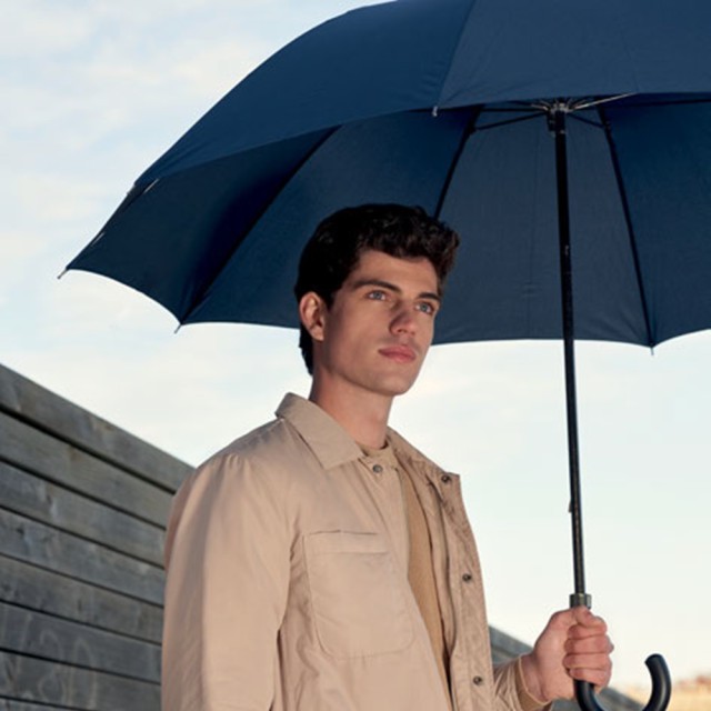 Długi parasol przeciwdeszczowy w dłoni mężczyzny.